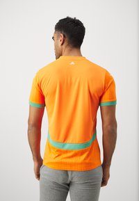 Korte mouw sportshirt in helder oranje met groene accenten, voorzien van een geregen patroon langs de zijkanten en achterkant, gemaakt van ademend materiaal.