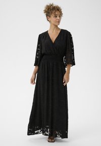 Fekete maxi ruha V nyakkivágással, átlátszó hímzett anyagból, háromnegyedes ujjal, és smockolt derékkal, amelynek laza szoknyája van.