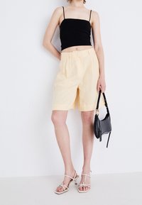 Bermuda di lino giallo chiaro con tasche laterali e vestibilità comoda, abbinate a un top cropped nero e a una piccola borsa a tracolla nera.