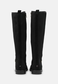 Bottes noires montantes jusqu'aux genoux présentant un tissu texturé avec des accents lisses, des fermetures éclair et une semelle basse profil.