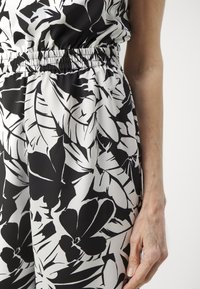 Tejido estampado en blanco y negro con grandes motivos florales y de hojas, con una cinturilla elástica y una textura suave.