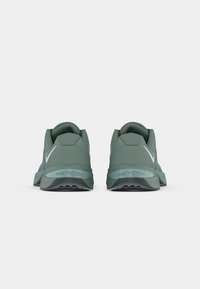 Grüne Sportschuhe mit einer strukturierten Oberseite, verstärkter Ferse und auffälligem "METCON" Branding auf der Sohle. Verfügt über weiße Akzente und ein niedriges Profil.