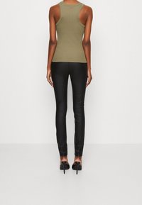 Olive green fitted tank top and black stretchy pants, both with a sleek, smooth texture. Heels elevate the overall look. Simple, modern design.