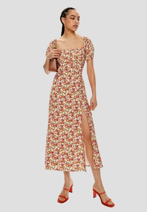 Vestido maxi floral en tejido ligero con mangas abullonadas, escote cuadrado, abertura lateral y detalles en rojo. Combinado con sandalias de tacón rojas.