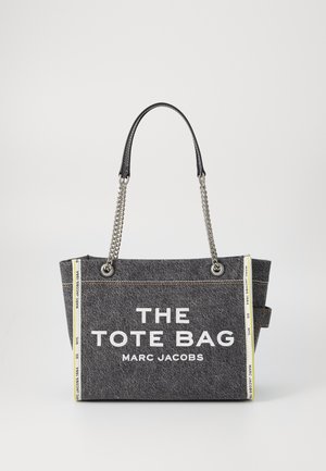 Grau getönte Stofftasche mit schwarzen Ledergriffen und silbernen Kettenakzenten. Auf der Vorderseite ist in weißer Schrift "THE TOTE BAG MARC JACOBS" zu lesen.