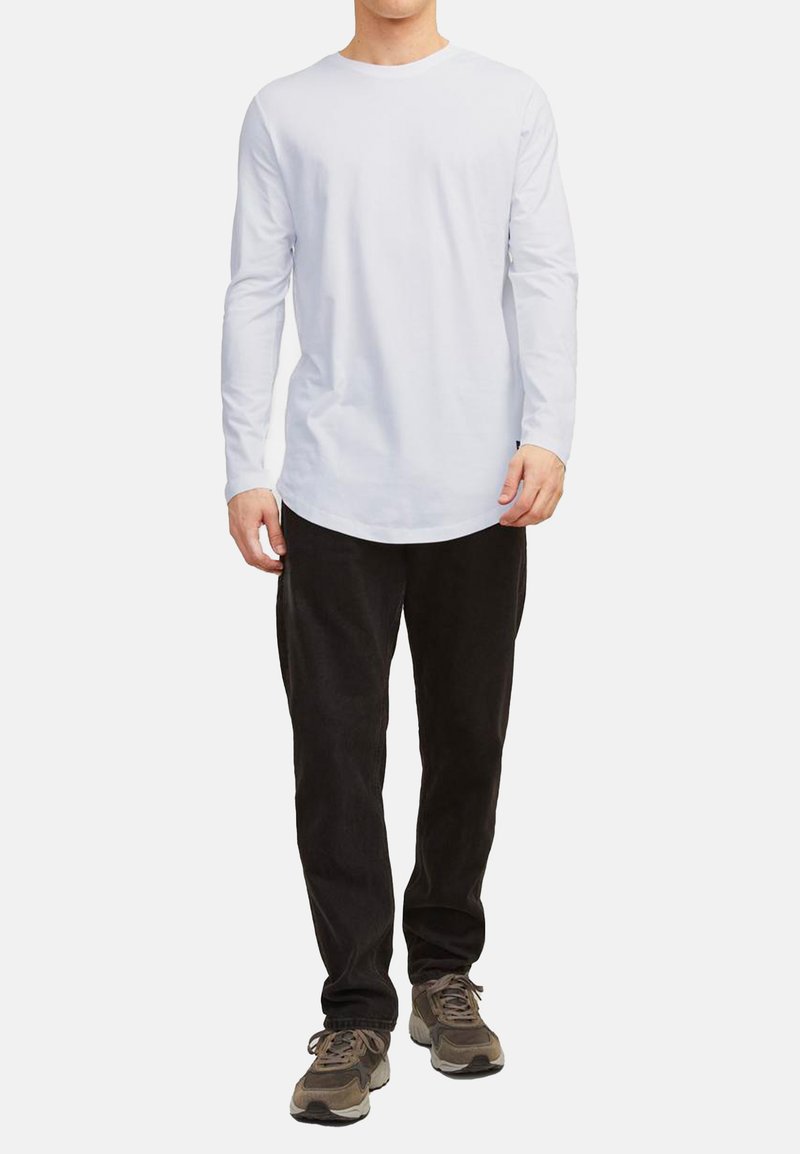 Chemise blanche à manches longues avec un col rond, associée à un pantalon noir et des baskets gris-brun ; présente une coupe décontractée et un design minimaliste.