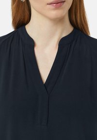 Granatowa bluzka z dekoltem w kształcie V, wykonana z miękkiego materiału, z subtelnymi zakładkami na ramionach, charakteryzująca się czystym i minimalistycznym wykończeniem dekoltu.