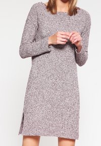 Stickad klänning i ett mjukt, spräckligt mönster med långa ärmar, rundad halsringning och sidslitsar vid nederkanten för ökad rörelsefrihet.