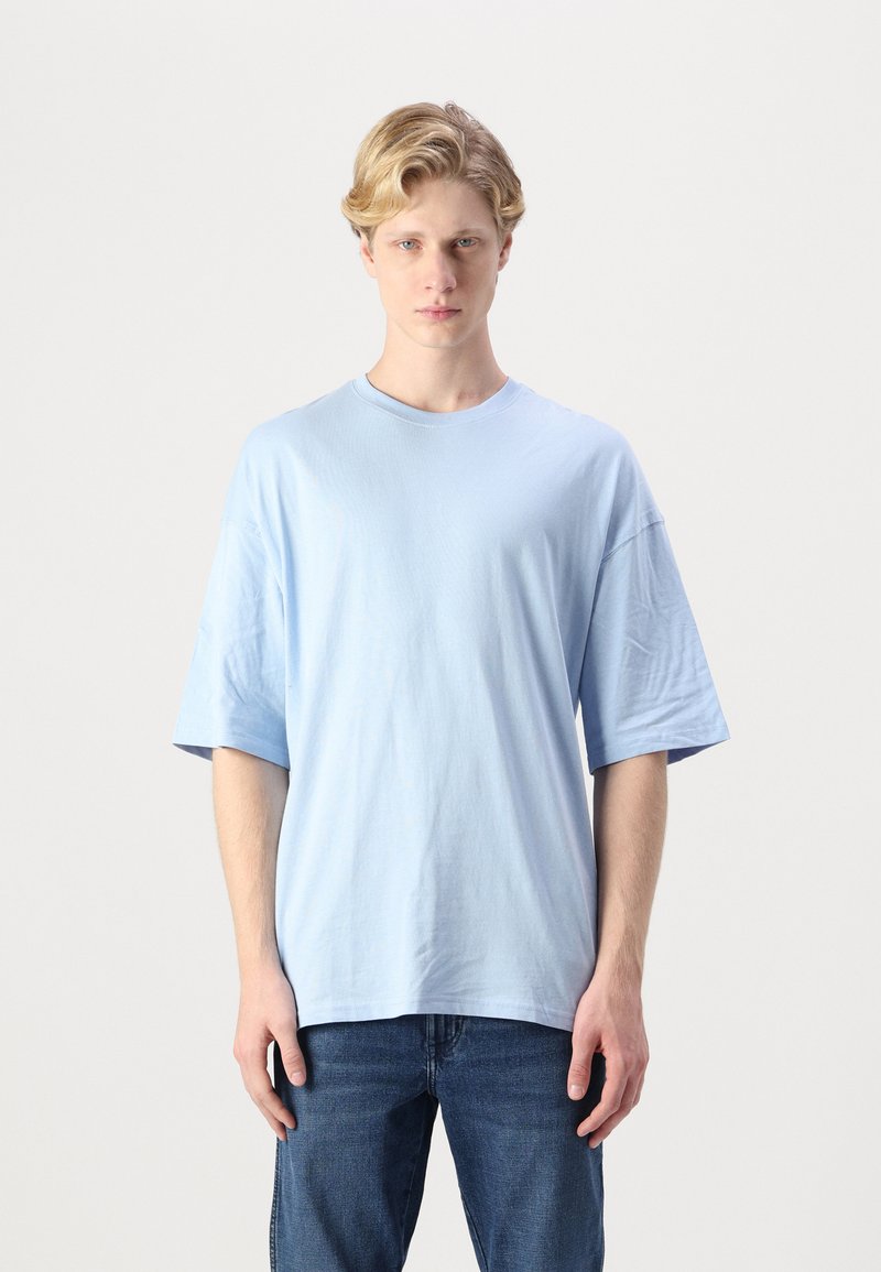 Light blue short-sleeve T-shirt made of soft fabric. Relaxed fit with a crew neck and no patterns. Paired with dark denim jeans.