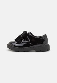 Schwarze Lacklederschuhe mit einer mattschwarzen Schleife und strukturierten Akzenten; runde Zehen und grobe Gummisohle für bessere Traktion.