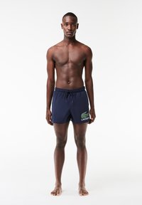 Shorts de bain bleus avec une taille élastique, cordon de serrage et logo Lacoste vert. Tissu lisse avec une coupe classique, longueur mi-cuisse.