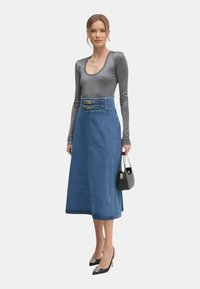 Jeans nederdel med høj talje, der har dobbelt spænde detaljer, kombineret med en tætsiddende metalisk langærmet top og sorte spidse hæle.