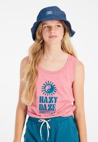 Top senza maniche rosa con stampa "HAZY DAZE" in blu, abbinato a pantaloni corti testurizzati color teal e un cappello a secchiello blu. Design morbido e casual.