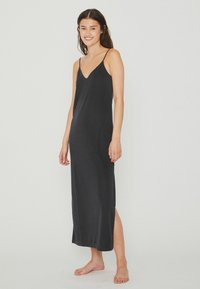 Robe maxi sans manches noire avec un décolleté en V, présentant une texture douce et des fentes latérales pour un confort de mouvement. Le tissu léger tombe élégamment.