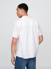 Hvit kortermet skjorte med broderte øyeletmønstre, bølgete kanter og krage, brukt med blå jeans.