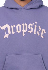Hoodie púrpura hecho de una tela suave que presenta un gran texto en estilo gótico de color rosa claro que dice "Dropsize" en la parte frontal, con un bolsillo delantero.