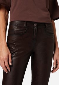 Bruine leren broek met een gladde textuur, voorzien van een vijfzakken ontwerp, subtiele stikdetails en een metalen knoopsluiting.