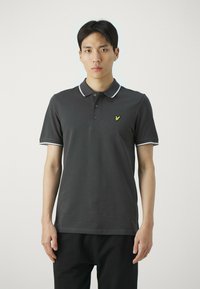 Polo shirt grigio scuro con colletto, patta con tre bottoni e rifiniture bianche. Presenta un piccolo logo giallo sul lato sinistro del petto. Texture liscia.