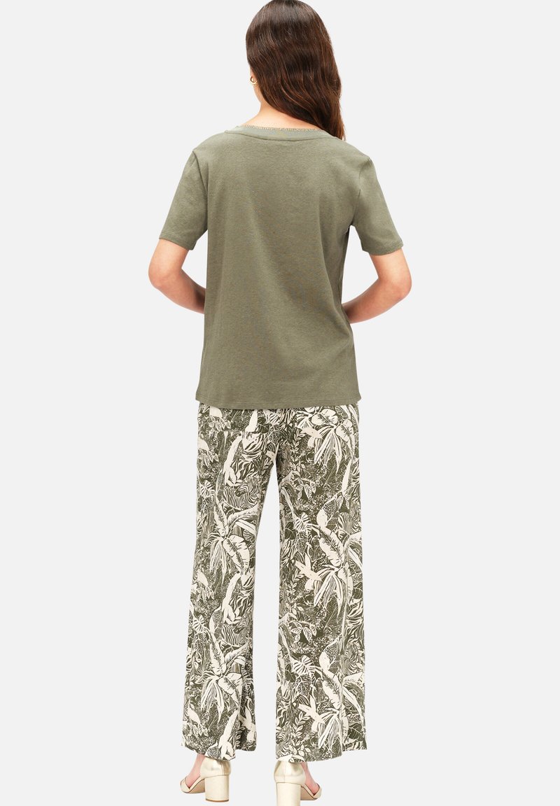 Olivgrünes T-Shirt mit kurzen Ärmeln, kombiniert mit weiten Hosen, die ein weißes botanisches Muster auf einem dunkelgrünen Hintergrund zeigen. Einfaches Design.