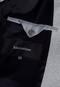 Svart och grå jacka med ett satinfinish invändigt, en grå knapp och en etikett med "Matinique" samt storleksinformation.