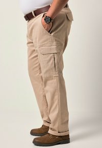 Pantalones cargo beige con bolsillos laterales, hechos de una tela suave, presentan un corte recto y puños doblados. Unos zapatos marrones de cordones completan el conjunto.