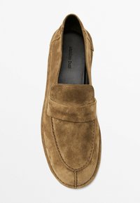Bruine suède instapper loafer met een gevoerd bandje, ronde neus en zichtbare stiksels langs de zool. Zachte textuur en minimalistisch ontwerp.