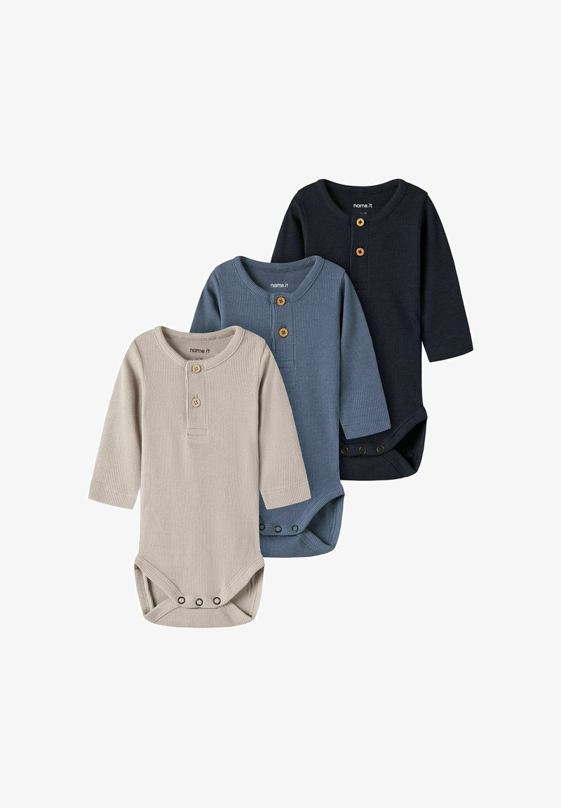 Trois bodies bébé à manches longues côtelés en beige, bleu et noir avec des boutons en bois sur la poitrine et des pressions en bas.