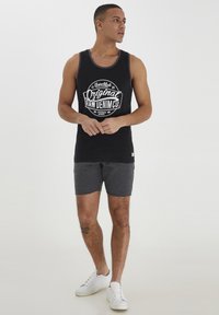 Black tank top with white graphic text, gray shorts, and white sneakers. Simple design, cotton material, well-fitted with a round neckline.