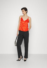 Top sem mangas vermelho com padrão de zebra texturizado, combinado com calças pretas de cintura alta com fendas na barra e sapatos de salto agudo.