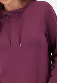 Paarse sweatshirt met een hoge hals, voorzien van metalen oogjes en een trekkoord. Zacht, gestructureerd materiaal met een losse pasvorm.