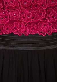 Klänning med en fuchsia blommig spetsbyst med paljetter, svart rynkad midja och en flödande svart kjol.