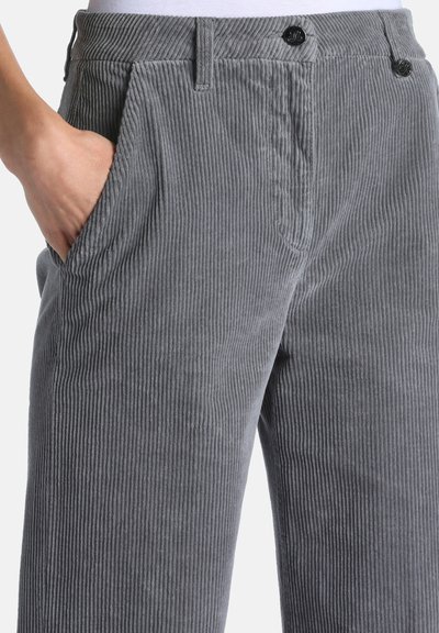 Main reposant dans la poche d’un pantalon en velours côtelé gris à côtes verticales avec fermeture à bouton et passants de ceinture.
