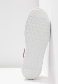 Semelle de chaussure blanche avec un motif hexagonal texturé, positionnée verticalement contre un mur d'angle blanc.