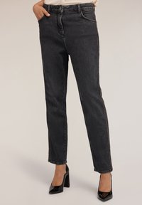 Jeans in denim nero con una vestibilità dritta, vita alta, cuciture tono su tono e dettagli con zip laterale. Abbinati a tacchi neri lucidi.