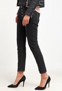 Svarta slim fit-jeans med hög midja, med framknappar, kontrasterande sömmar och en jämn denimtextur, i kombination med svarta högklackade skor.