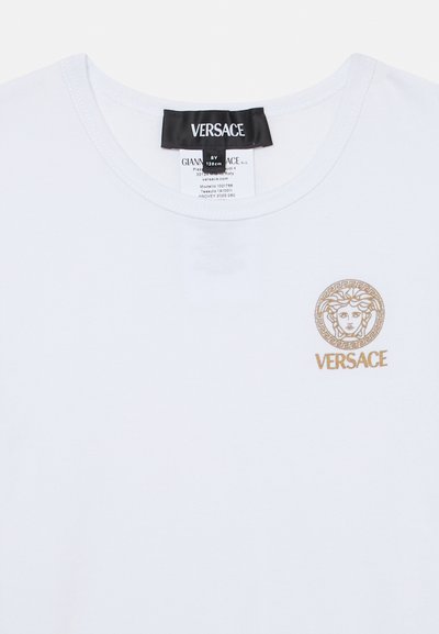 Valge Versace T-särk ümar kaelusega, kuldse Medusa logoga ja „VERSACE“ tekstiga ülemisel vasakul rinnal.