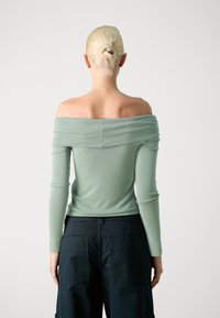 Mintgrön avskuren topp med långa ärmar, gjord av mjukt material. Har ett rynkat tyg vid halsringningen och en figursydd midja.