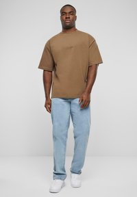 Hnedé oversized tričko s krátkymi rukávmi, vybavené jemným logom, kombinované s svetlomodrými rovnými nohavicami a bielymi teniskami.