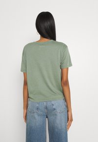 Grön bomullströja med korta ärmar, rund halsringning och rak nederkant. Buren tillsammans med ljusblå, högmidjade denimjeans.