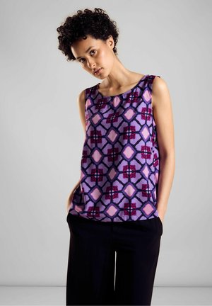 Blusa viola senza maniche con un motivo geometrico in accenti rosa e rossi. Tessuto morbido con una vestibilità rilassata. Abbinata a pantaloni neri.