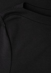 Czarna tkanina ukazująca dwie nachodzące na siebie części, charakteryzujące się gładką fakturą i okrągłym dekoltem. Szwy widoczne są wzdłuż krawędzi.