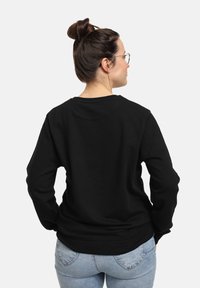 Felpa nera in cotone con maniche lunghe, scollatura a girocollo e polsini a costine. Indossata con jeans in denim azzurro chiaro, vista da dietro.