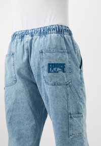 Világoskék farmer cargo nadrág, rugalmas derékkal, két oldalsó zsebből és hímzett "FORCE" logóból a hátsó zseben.