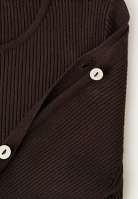 Top tricotat cu nervuri de culoare maro, cu un gât rotund, având un detaliu cu nasture pe lateral. Textură netedă cu linii verticale subtile.