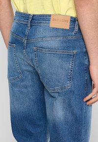 Jeans de mezclilla azul claro con un ajuste relajado, que cuentan con un parche de cuero en la cinturilla trasera y dos bolsillos traseros.