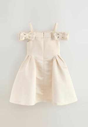 Kremowa sukienka odsłaniająca ramiona z dwoma dużymi kokardami na ramionach, plisowana spódnica i zapięcie na suwak z tyłu. Gładka faktura materiału.