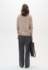 Pull en maille beige à manches longues, associé à un pantalon gris ample. La personne tient un sac fourre-tout en cuir brun foncé.