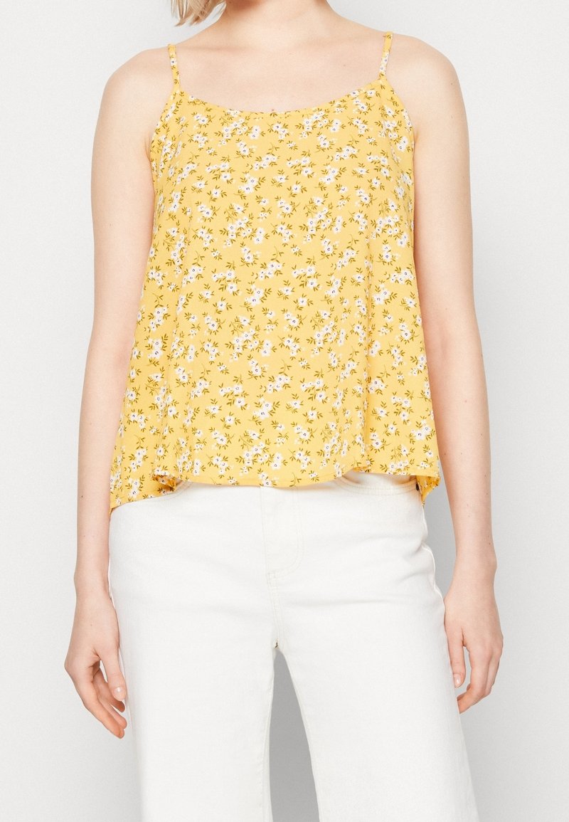 Top de tirantes finos en color amarillo con flores, que presenta un corte holgado y pequeños patrones florales en blanco y rosa sobre una tela texturizada.