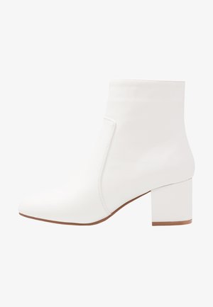 White ankle boots with a smooth finish, square toe, and a mid-height block heel. Seam detailing accentuates the minimalist design.