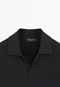 Polo noir en maille avec un col plié et un col en V ouvert, montrant une étiquette Massimo Dutti à l'intérieur de l'encolure.